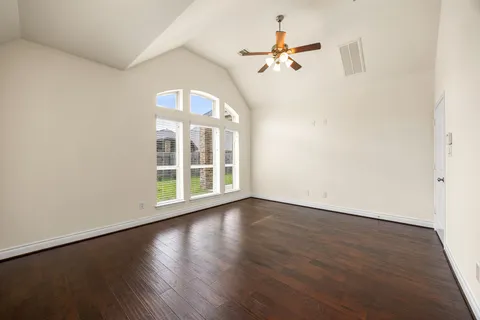 an empty room with wooden floor fan and windows