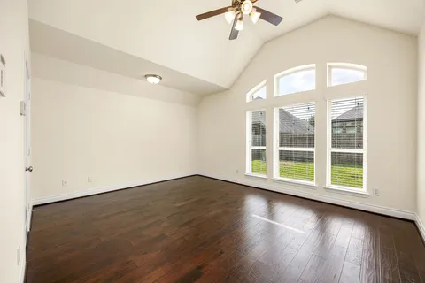 an empty room with wooden floor fan and windows