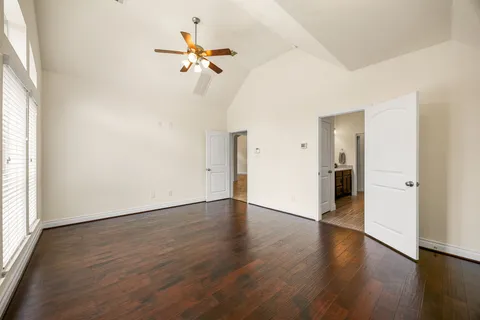 an empty room with wooden floor fan and windows