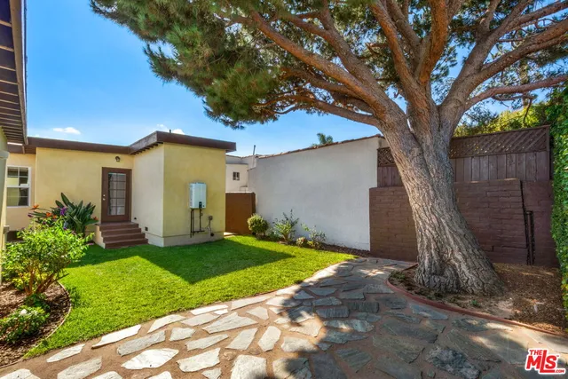 a backyard of a house with plants and large tree