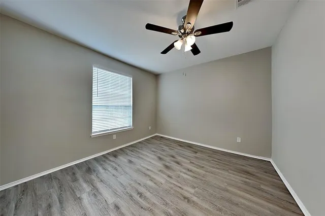 an empty room with wooden floor fan and windows