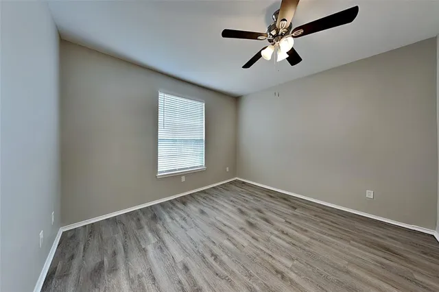 an empty room with wooden floor chandelier fan and windows