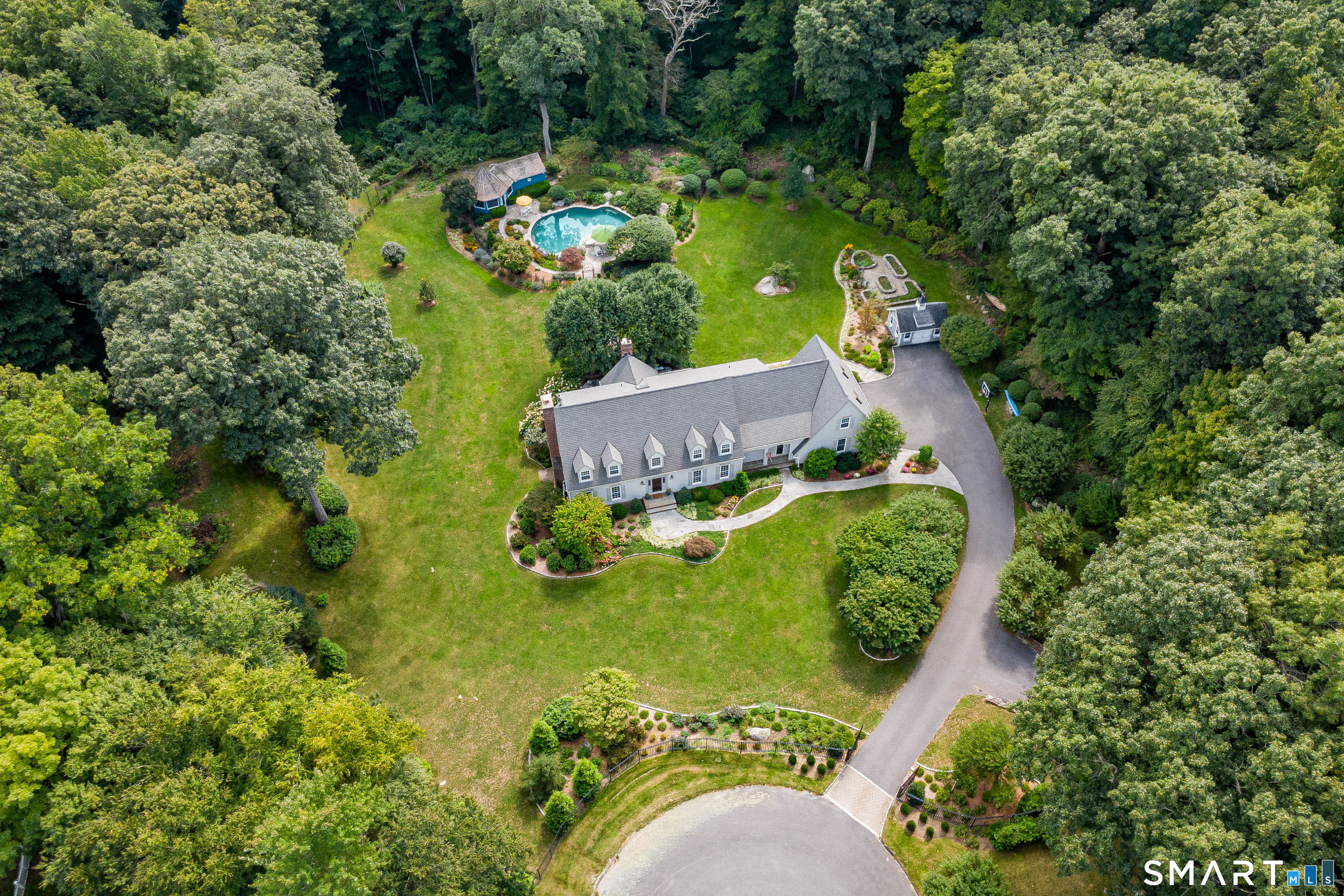 Aerial view showcasing the home, expansive grounds, circular driveway, pool area and surrounding mature trees.