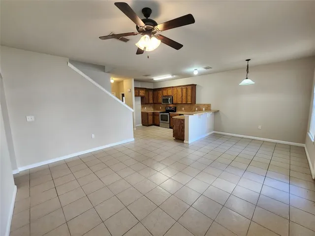 an empty room with kitchen view and a ceiling fan