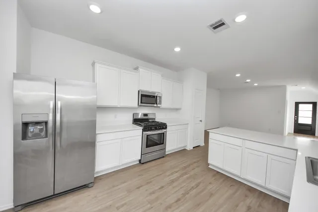 a kitchen with stainless steel appliances kitchen island granite countertop a refrigerator a sink a stove and white cabinets with wooden floor