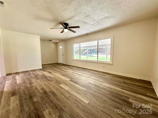 an empty room with wooden floor ceiling fan and windows