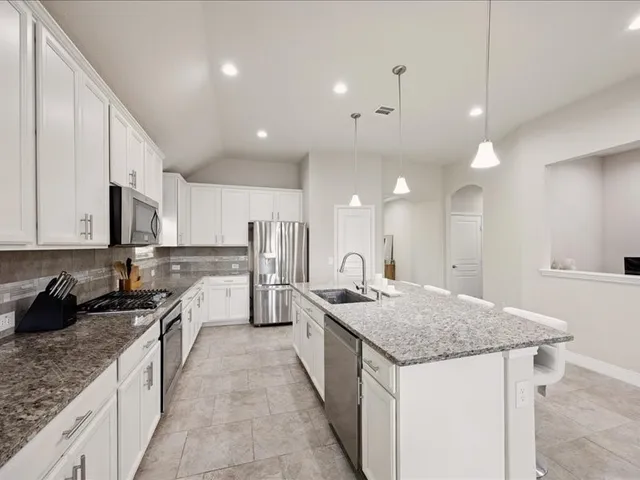 a kitchen with stainless steel appliances granite countertop a sink a stove top oven a refrigerator and white cabinets