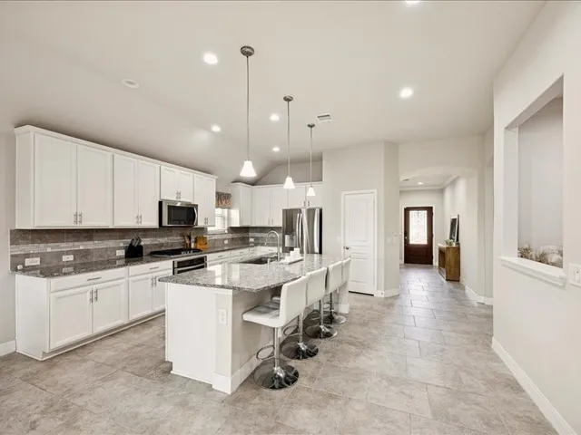 a kitchen with stainless steel appliances granite countertop a stove top oven a sink a refrigerator a dining table and chairs