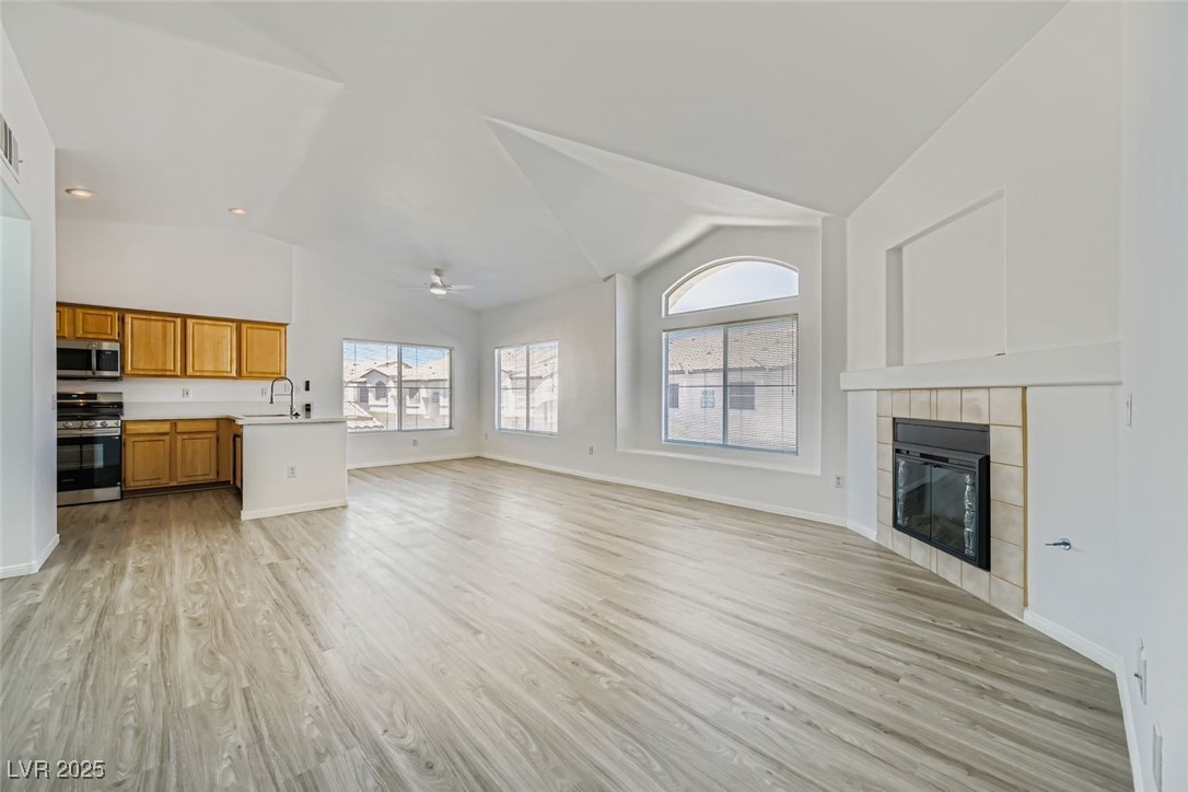 4941 Black Bear Road, Unit 203 Las Vegas, NV 89149 - Photo 2 of 11 Unfurnished living room featuring light wood-style floors, a tiled fireplace, a ceiling fan, recessed lighting, and high vaulted ceiling