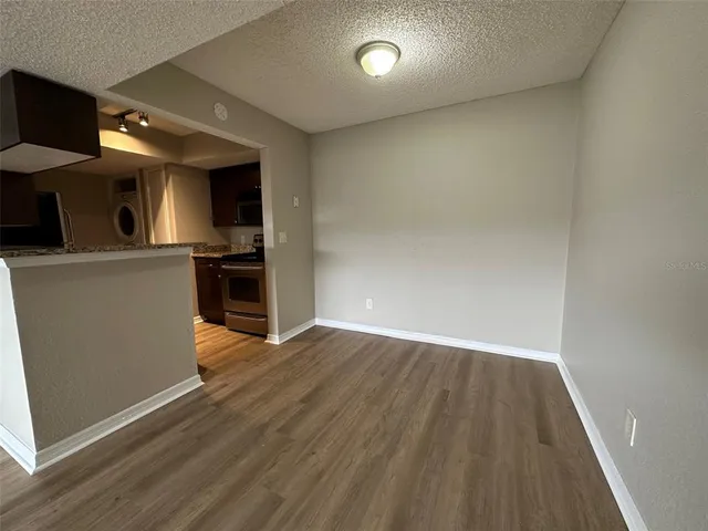 an empty room with wooden floor kitchen view and a window