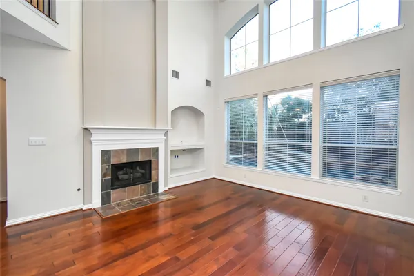 an empty room with wooden floor fireplace and windows