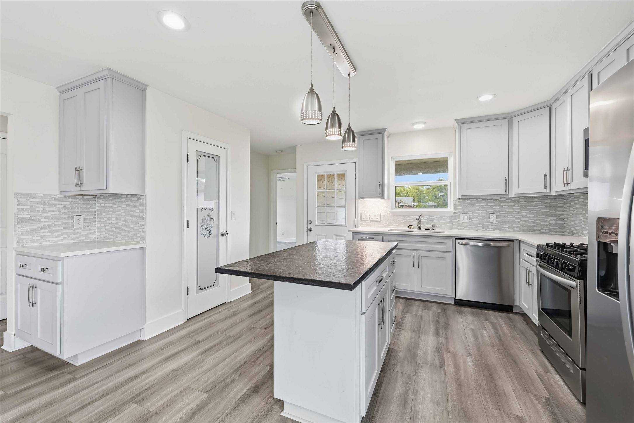 400 Booth Street Taylor, TX 76574 - Photo 14 of 35 Kitchen with stainless steel appliances, a center island, tasteful backsplash, decorative light fixtures, and light wood-style floors