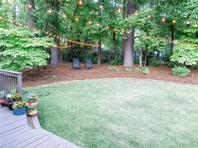 a view of a backyard with table and chairs potted plants and large tree