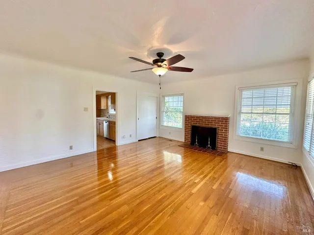 an empty room with wooden floor fireplace and windows