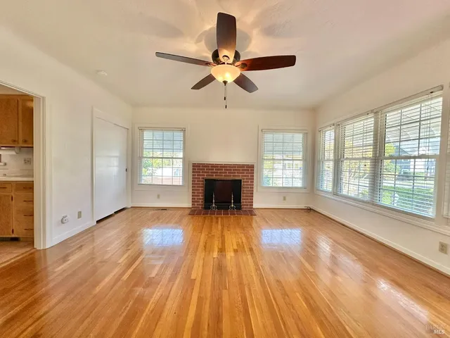 an empty room with wooden floor a ceiling fan and windows