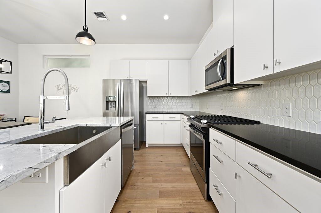5212 Huisache Street, Unit 2 Austin, TX 78751 - Photo 11 of 30 Kitchen featuring white cabinetry, stainless steel appliances, dark stone counters, light wood finished floors, and hanging light fixtures