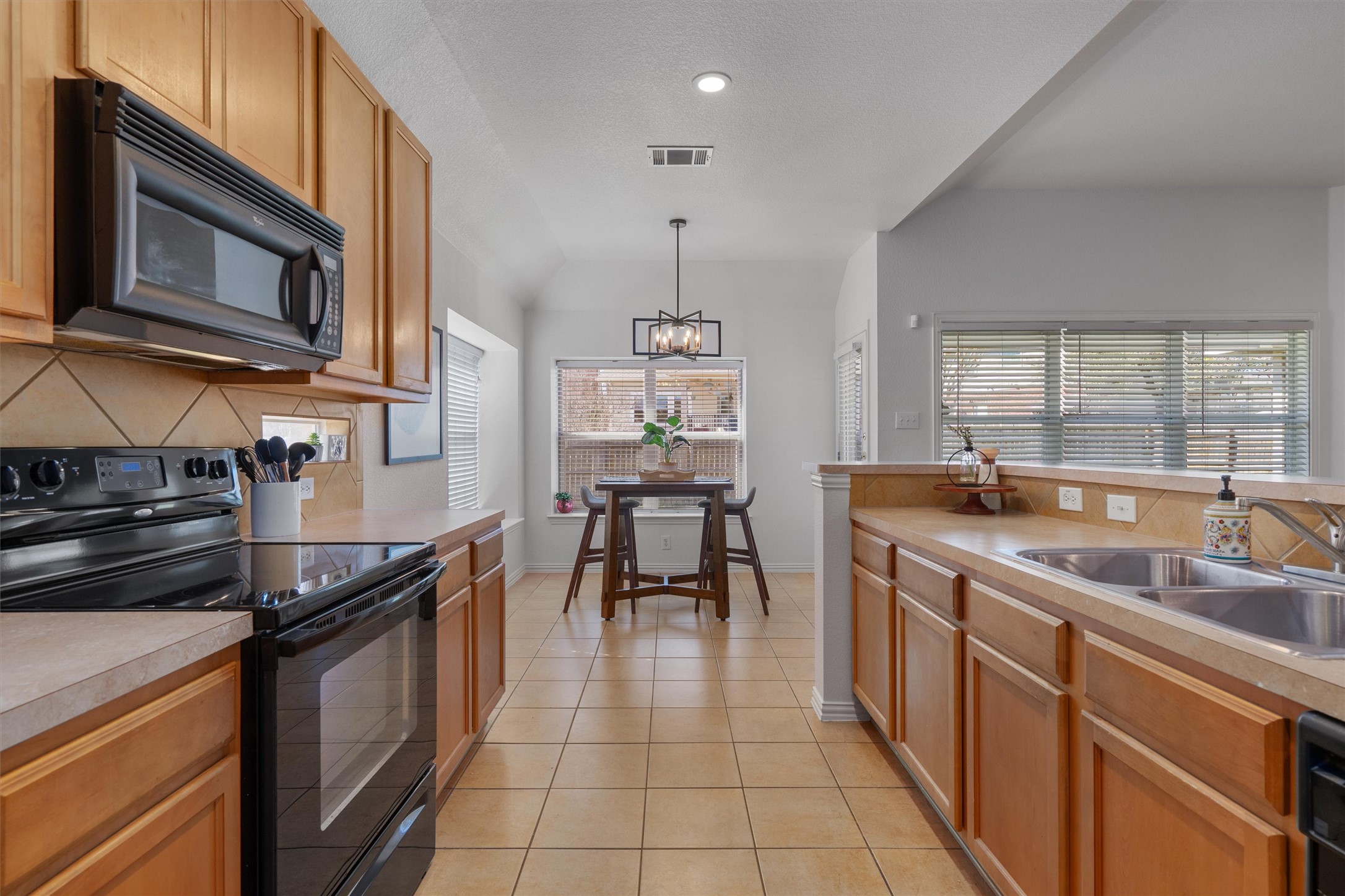 2801 Kickapoo Cavern Drive Pflugerville, TX 78660 - Photo 17 of 38 Kitchen with black appliances, light countertops, backsplash, light tile patterned floors, and suspended lighting