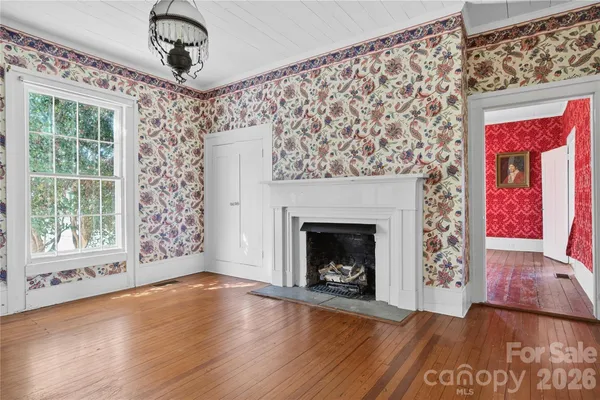 a view of an empty room with wooden floor fireplace and a window