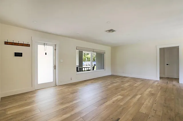 a view of an empty room with wooden floor and a window