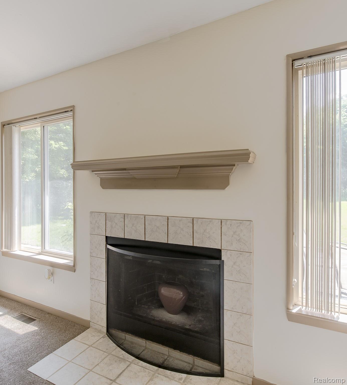 312 Reid Road Highland, MI 48357 - Photo 10 of 47 Fireplace featuring a decorative mantelpiece, light-toned tile surround, and an integrated fire screen