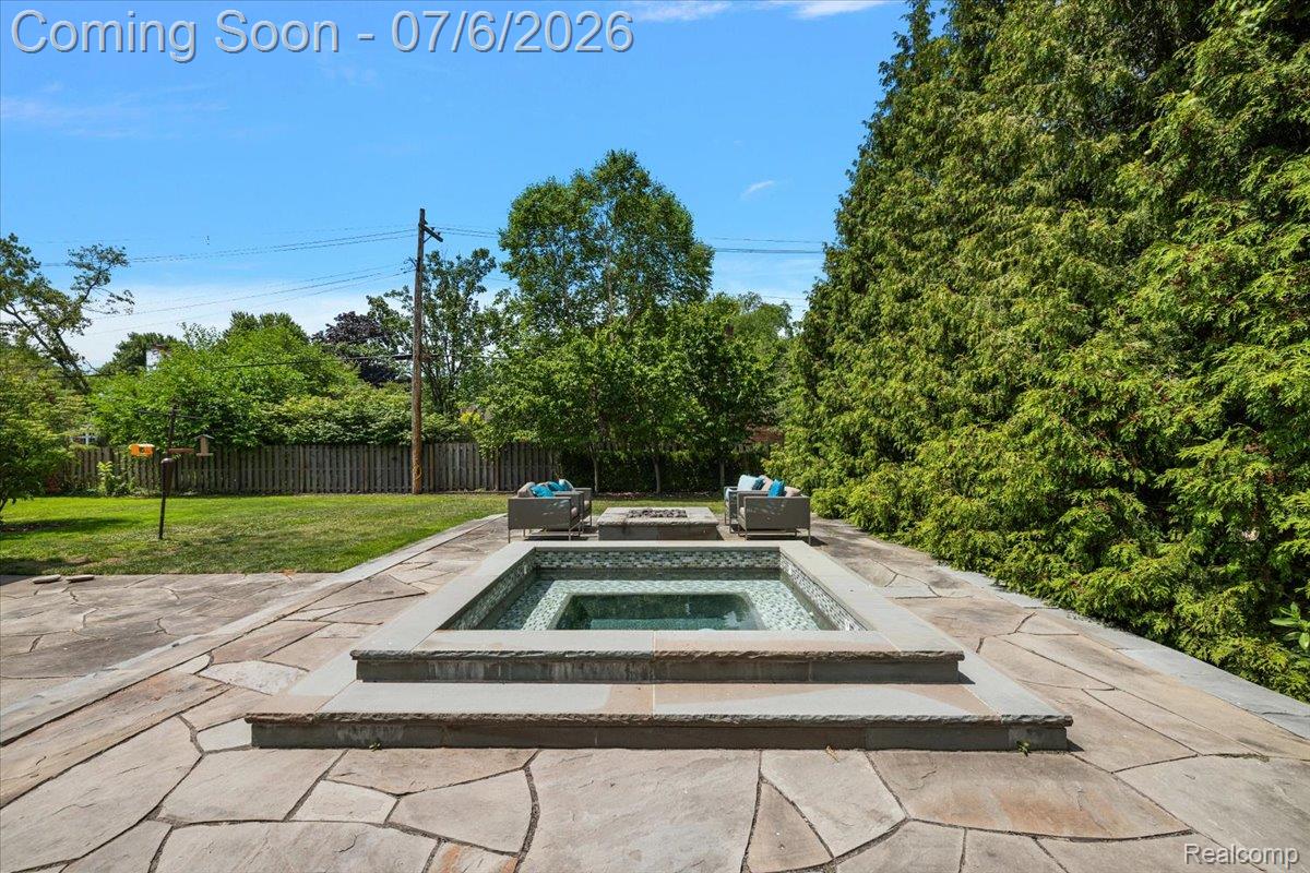 1051 Devonshire Road Grosse Pointe, MI 48230 - Photo 82 of 98 Landscaped backyard featuring an in-ground square spa surrounded by a flagstone patio, a rectangular fire pit, and a backdrop of mature evergreen trees