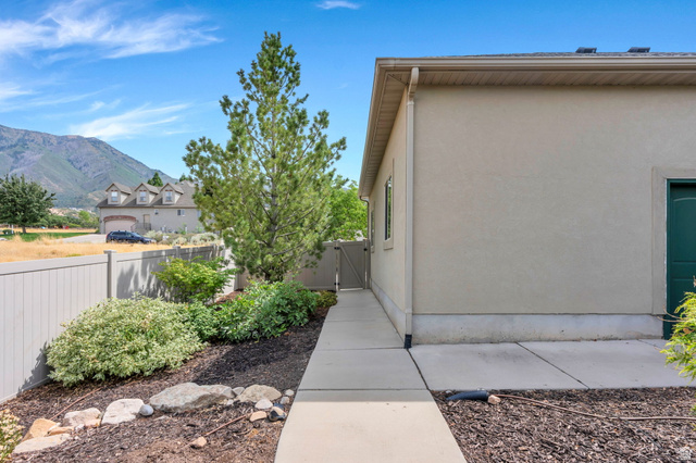 373 East Alexander Drive Elk Ridge, UT 84651 - Photo 55 of 69 Stucco exterior with a side walkway leading to a gate, mature trees, and established landscaping