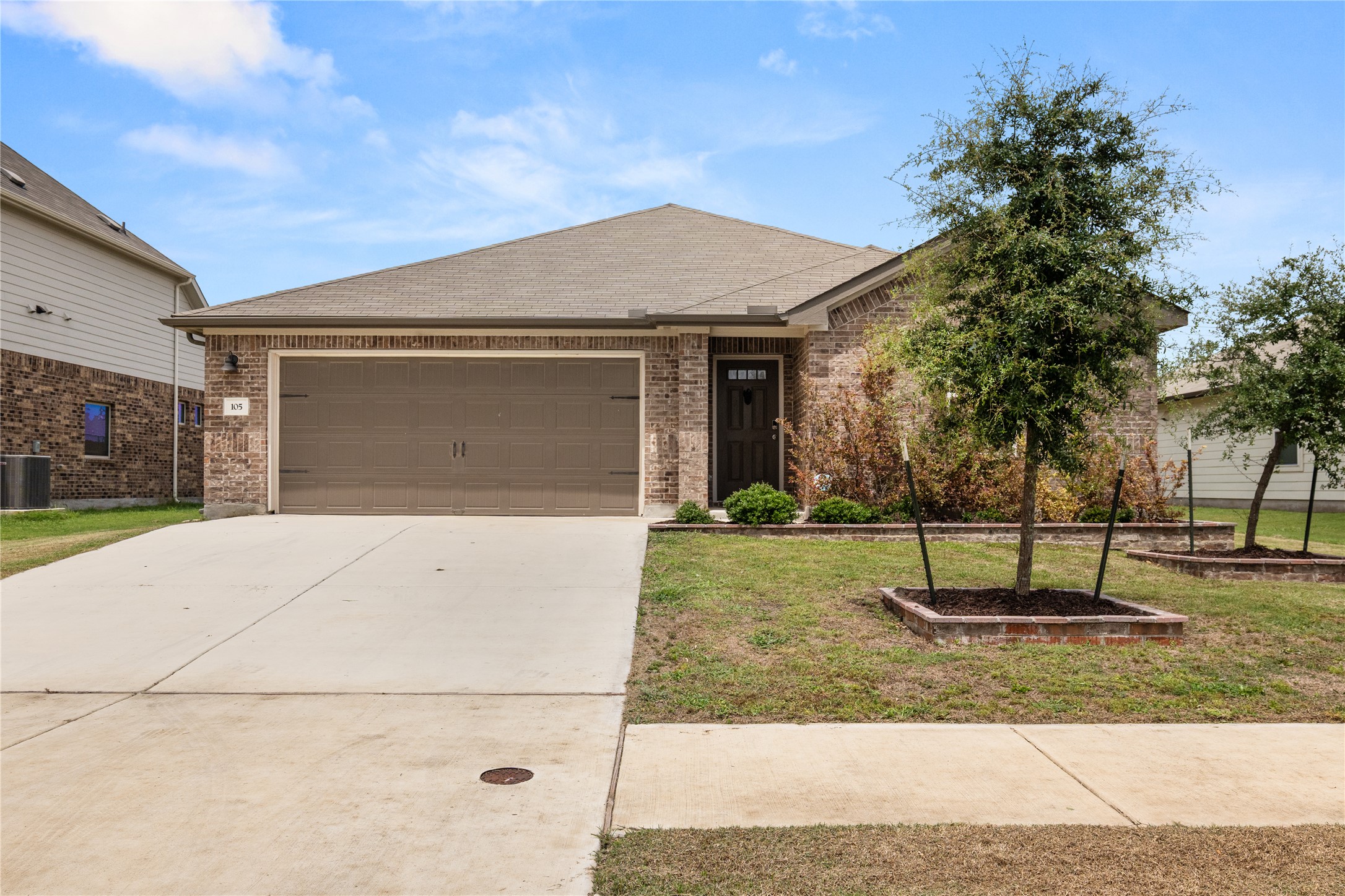 105 Saviano Road Hutto, TX 78634 - Photo 1 of 22 A charming single-story residence boasts a brick facade and an inviting front yard with young trees.