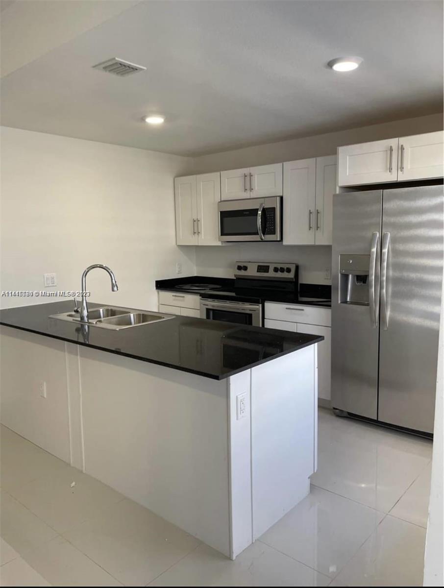 13966 Southwest 258th Street, Unit 13966 Homestead, FL 33032 - Photo 2 of 5 a kitchen with stainless steel appliances granite countertop a sink a stove a refrigerator a microwave and cabinets