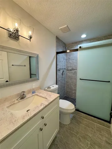 a bathroom with a granite countertop sink a toilet a mirror a vanity and shower