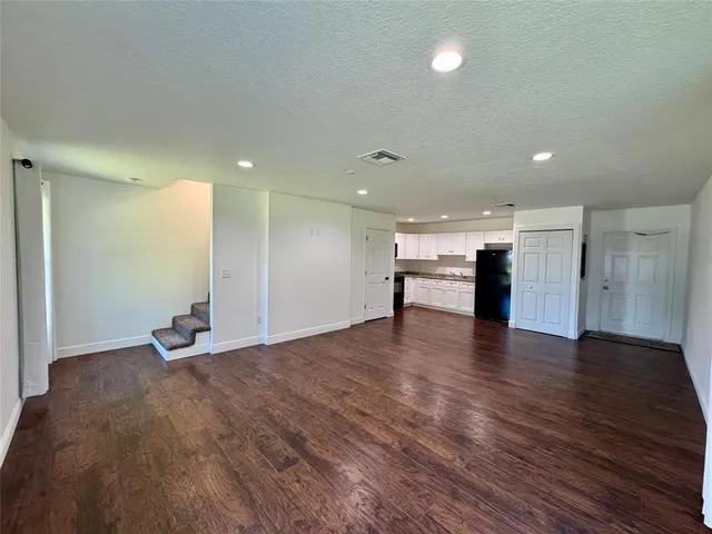a view of an empty room with wooden floor and a kitchen