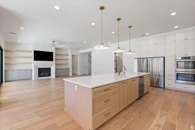 1192 East Corral Way Washington, UT 84780 - Photo 20 of 81 Open-concept living space featuring wood-finish flooring, a kitchen island with pendant lighting, stainless steel appliances, extensive white cabinetry, and a fireplace with built-in shelving and cabinetry