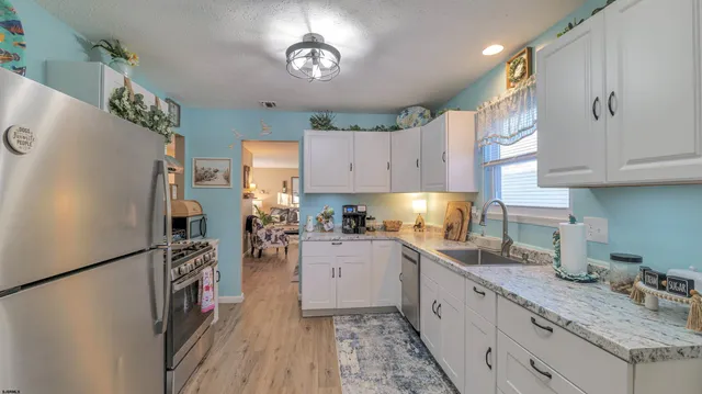 a kitchen with granite countertop a refrigerator a sink dishwasher stove and white cabinets