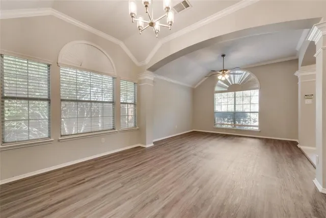 an empty room with wooden floor chandelier and windows
