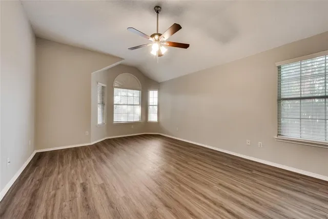 an empty room with wooden floor chandelier fan and windows