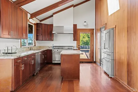 a kitchen with stainless steel appliances granite countertop a stove top oven a sink dishwasher and a refrigerator with wooden floor