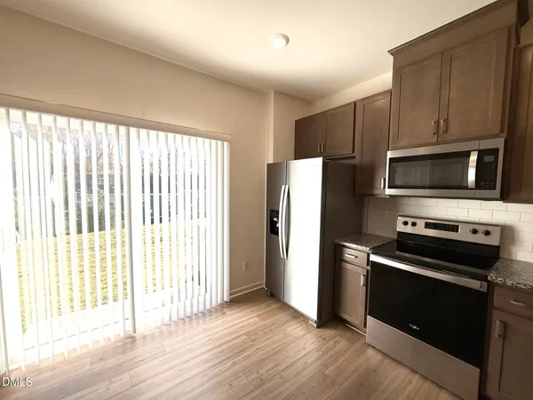 an empty room with wooden floor and a kitchen