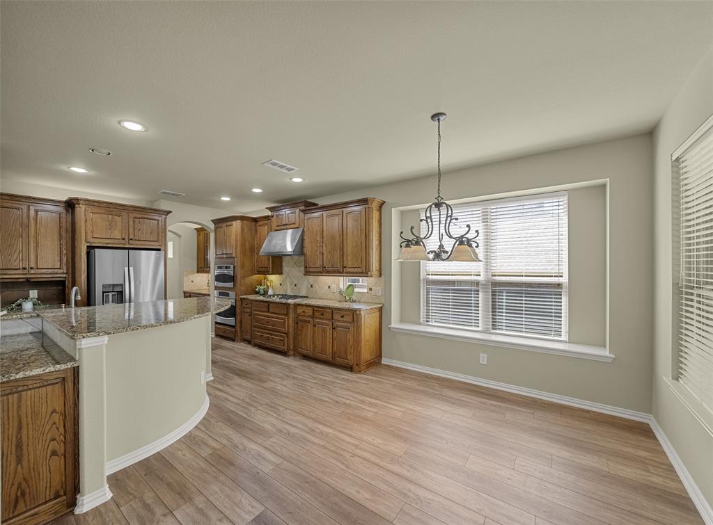 5143 Stream Crest Way Fairview, TX 75069 - Photo 11 of 35 Kitchen with wood finish cabinetry, arched walkways, hanging lights, and light stone counters
