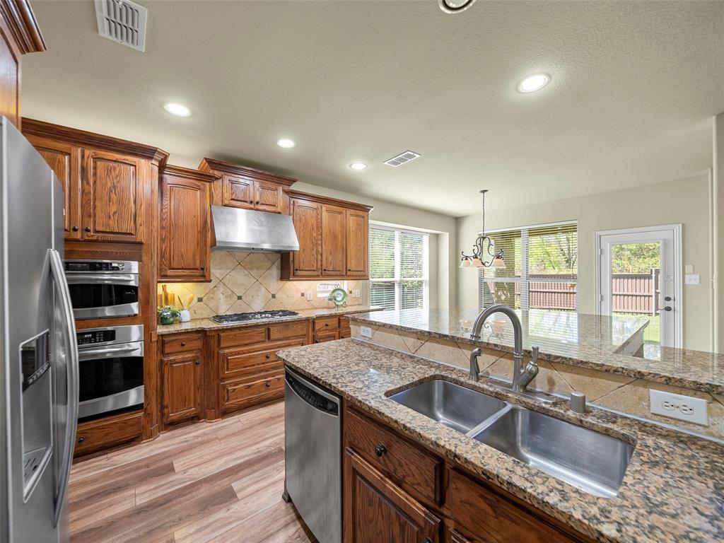 5143 Stream Crest Way Fairview, TX 75069 - Photo 12 of 35 Kitchen with wood finish cabinets, stainless steel appliances, light wood finished floors, and light stone countertops
