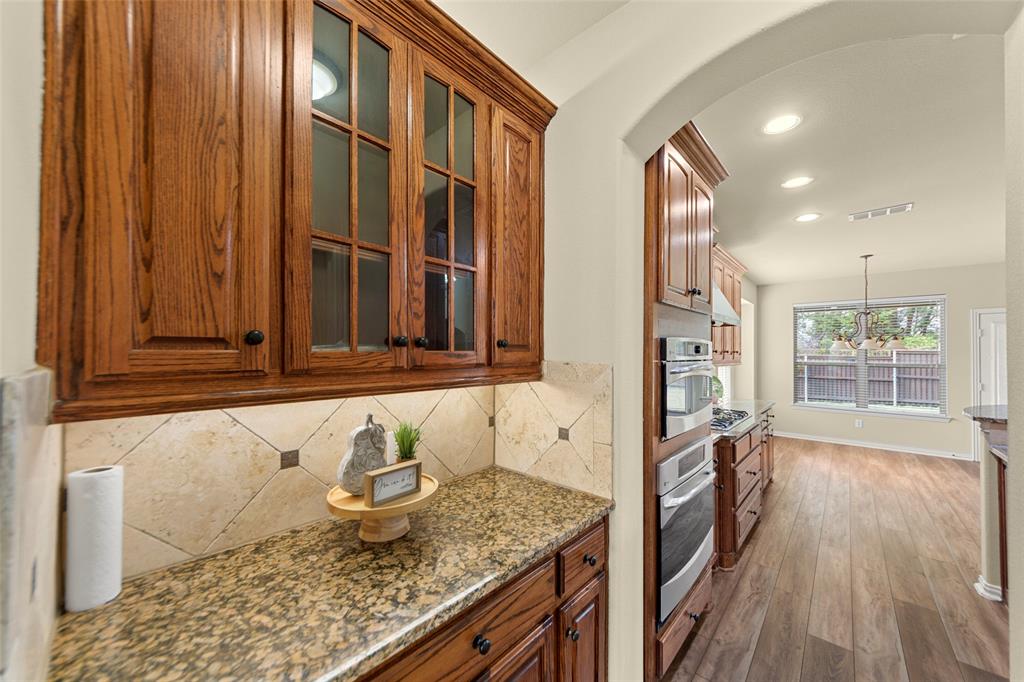 5143 Stream Crest Way Fairview, TX 75069 - Photo 14 of 35 Kitchen featuring light stone counters, wood finish cabinetry, wood finished floors, glass fronted cabinets, and arched walkways