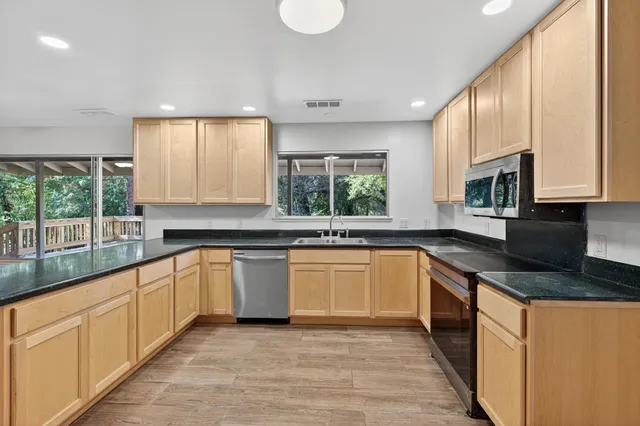 a large kitchen with stainless steel appliances granite countertop a stove a sink and a granite counter tops with a large window