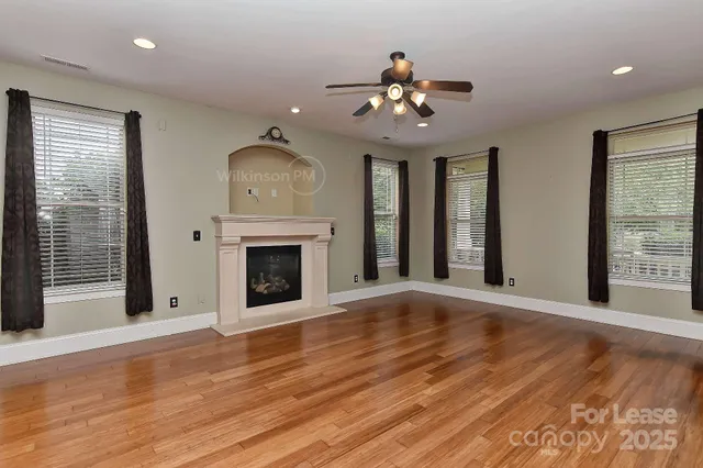 a view of an empty room with wooden floor fireplace and a window
