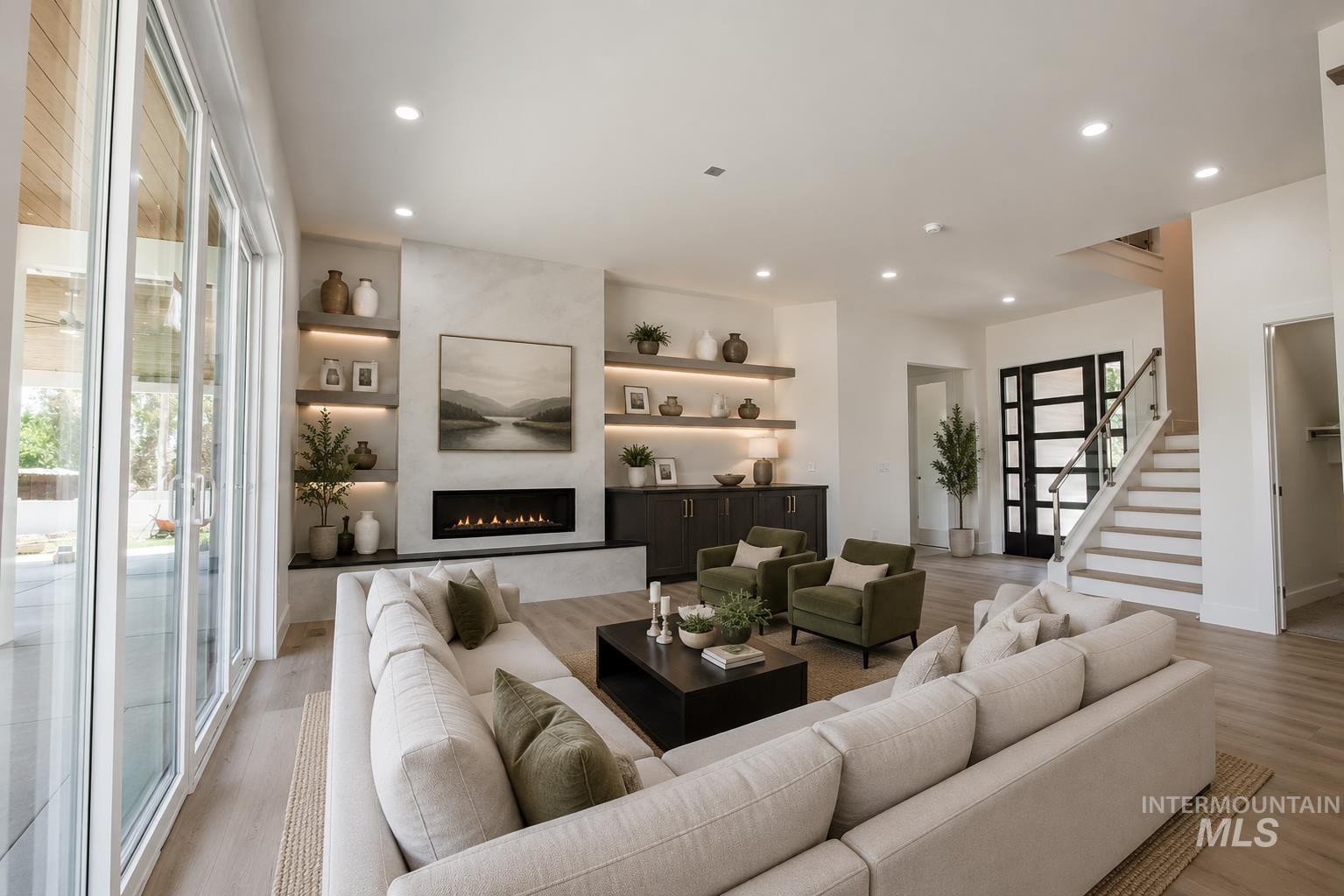 23904 Southview Lane Middleton, ID 83644 - Photo 5 of 29 Open-concept living space featuring a linear gas fireplace with built-in shelving, wood-finish flooring, a contemporary staircase with glass railing, recessed lighting, and large sliding glass doors