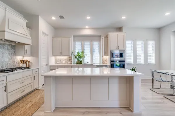 a kitchen with kitchen island granite countertop a stove a sink a refrigerator and white cabinets with wooden floor