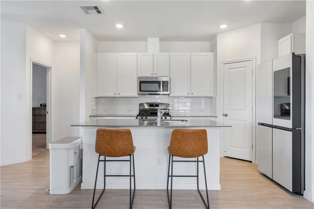 a kitchen with stainless steel appliances granite countertop a stove a refrigerator a microwave a sink and white cabinets with wooden floor