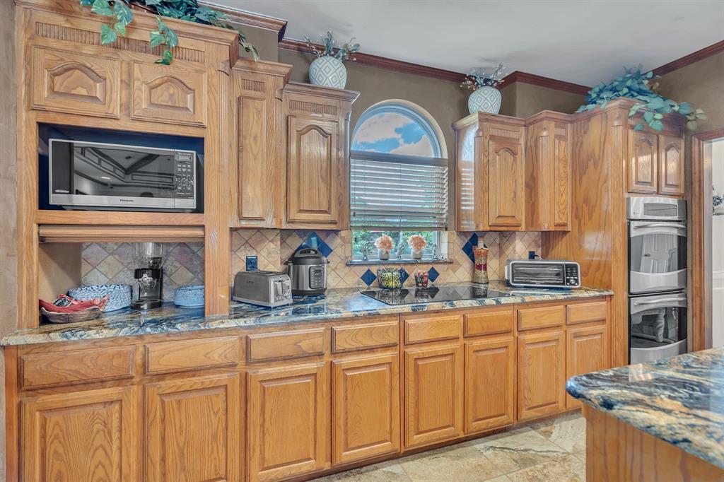 50 Buckingham Lane Allen, TX 75002 - Photo 23 of 39 Kitchen with appliances with stainless steel finishes, backsplash, dark stone countertops, crown molding, and brown cabinetry