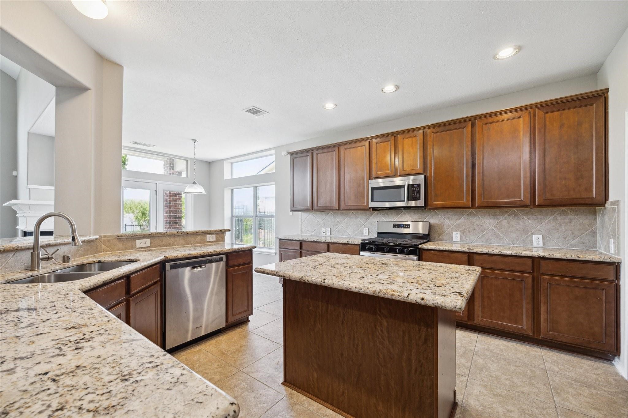 30507 Russell Point Drive Spring, TX 77386 - Photo 11 of 33 This spacious kitchen features granite countertops, stainless steel appliances, and ample wooden cabinetry. It has an open layout with a central island, tile flooring, and plenty of natural light flowing in from large windows.