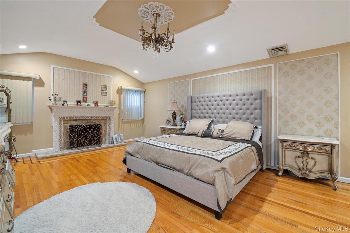 626 Caledonia Road Dix Hills, NY 11746 - Photo 26 of 50 Bedroom with light wood-type flooring, recessed lighting, a chandelier, a fireplace with raised hearth, and lofted ceiling