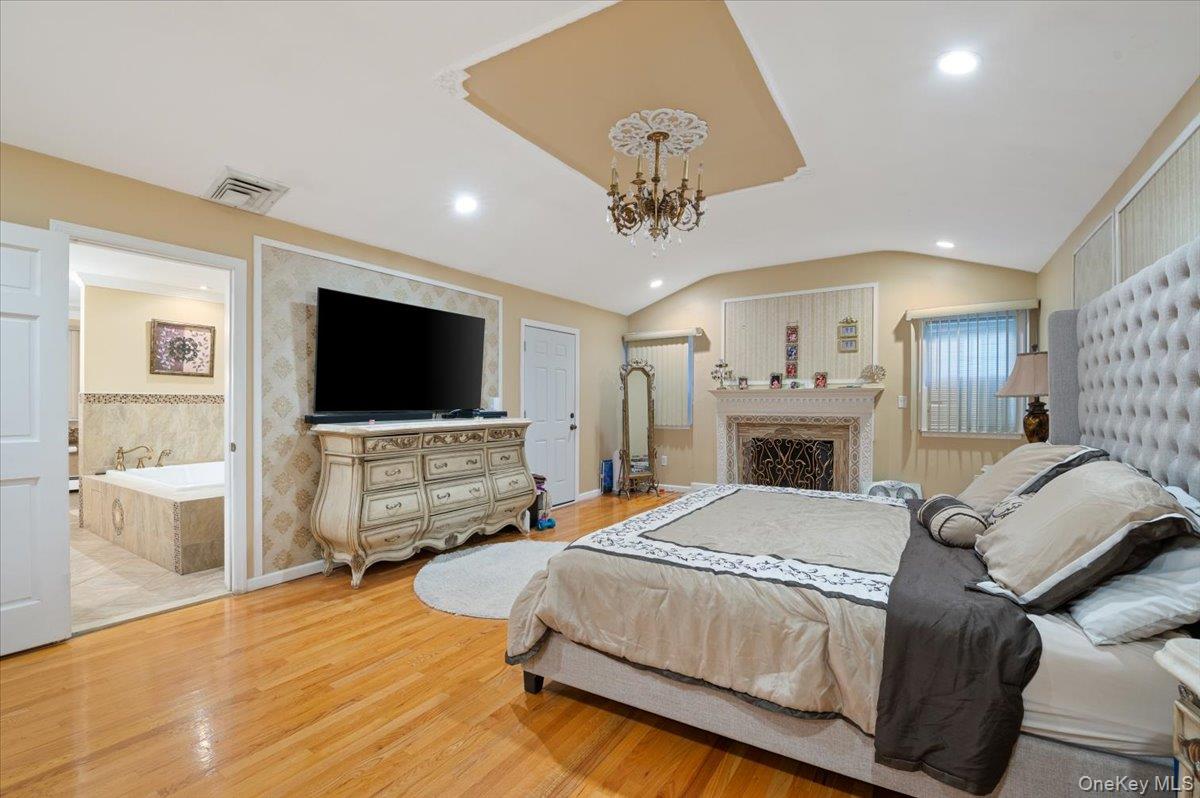 626 Caledonia Road Dix Hills, NY 11746 - Photo 27 of 50 Bedroom with wood finished floors, vaulted ceiling, a chandelier, recessed lighting, and a fireplace
