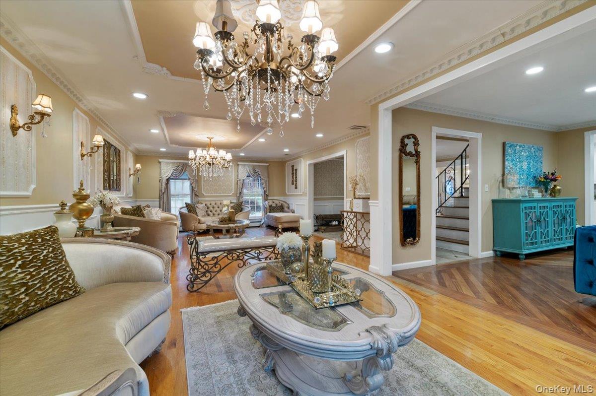 626 Caledonia Road Dix Hills, NY 11746 - Photo 10 of 50 Living room featuring crown molding, a raised ceiling, a chandelier, stairs, and wood finished floors