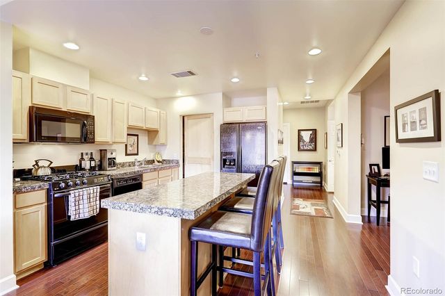 a kitchen with stainless steel appliances granite countertop a refrigerator a stove top oven a sink dishwasher and white cabinets with wooden floor